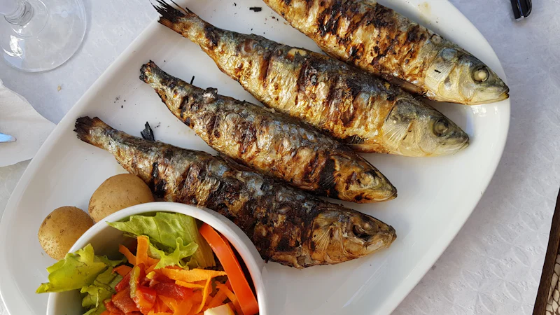 Cá nhỏ nướng nguyên con bày trên đĩa trắng ăn kèm salad rau