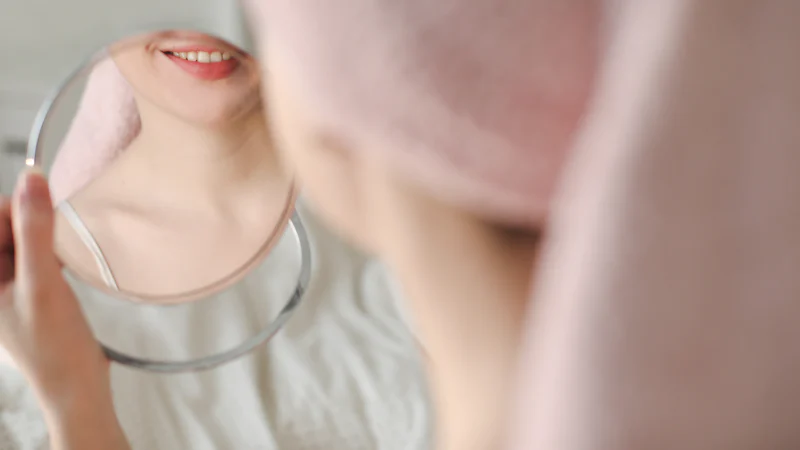Phụ nữ quấn khăn trên đầu soi gương chăm sóc da mặt