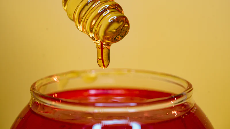 Mật ong chảy từ que gỗ xuống hũ thủy tinh