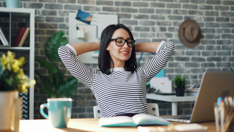 Người phụ nữ ngồi làm việc trước máy tính trong văn phòng, vươn tay ra sau đầu để thư giãn