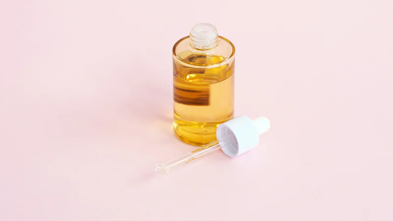 Lọ serum thủy tinh kèm ống nhỏ giọt đặt trên mặt phẳng màu hồng nhạt
